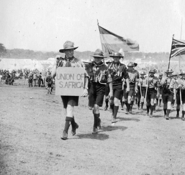 Scouts in uniforms marching with flags and a sign reading "Union of S. Africa"