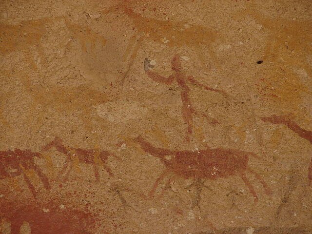 Cave painting with red pigment showing animal figures and a person. 