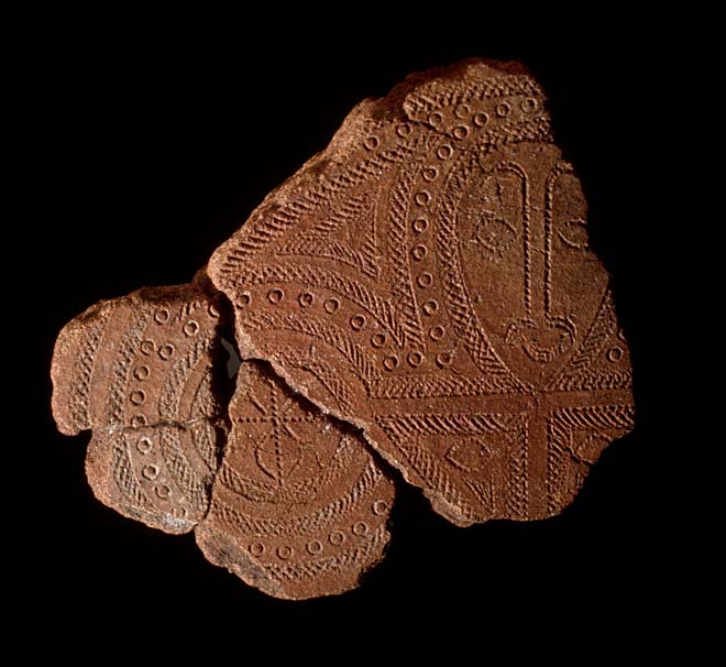 Three reddish-brown fragments of potter featuring a human face and geographic patterns. 