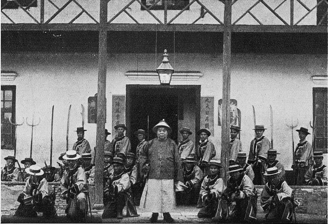 Photograph of about 20 soldiers posing in front of a building