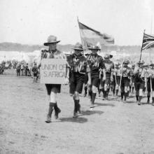 Scouts in uniforms marching with flags and a sign reading "Union of S. Africa"