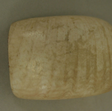 A light colored, rectangular bead with small, stripe-like markings. 