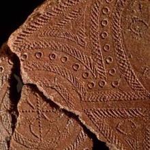 Three reddish-brown fragments of potter featuring a human face and geographic patterns. 