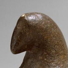 A brown-colored, stone figure loosely in the shape of a bird with a beak and two small wings. 