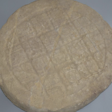 A light-colored limestone altar. The altar is round and has glyph blocks in the center that are word and faded. Two cracks are on the altar but have had repairs lessening the lines. 