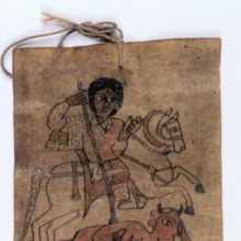 The top of a healing scroll; the paper is brown and there is a drawing of a saint riding a horse and using a spear to destroy a demon. There is a hole with a rope through the top of the scroll. 