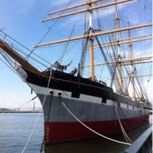 Photograph of a ship with three masts tied to a dock.