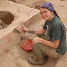 A woman kneels and holds a piece of stone at an archeological site 